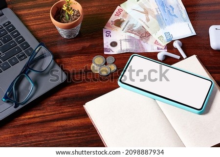 Desk, home office, computer and notebook, man working, calculating taxes. Glasses on computer and wooden desk. Mexican banknotes. Cell phone mock up.