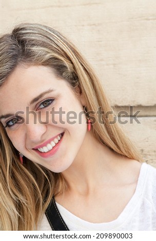 Close up portrait of an attractive young woman relaxing outdoors, smiling and looking at the camera with joyful friendly expressions. Young people lifestyle.