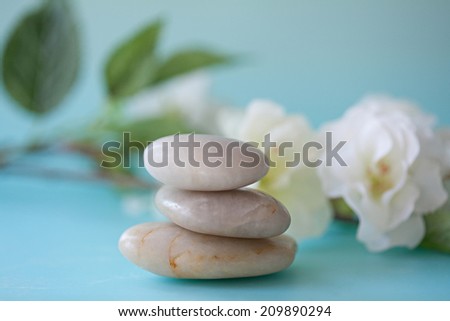 Close up still life detail view of a pile of natural smooth white stones balancing in a stack against white blossom flowers in a blue health spa background. Nature objects and zen energy.