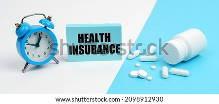 Medicine and health concept. On a blue surface are pills, on a white surface an alarm clock and a plate with the inscription - HEALTH INSURANCE