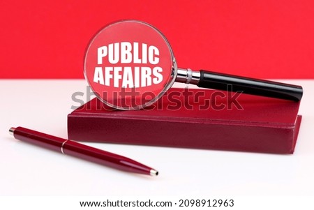 Business and finance concept. On a white and red background, a notebook, a pen and a magnifying glass, inside which the inscription - Public Affairs