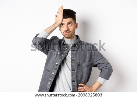 Annoyed young man looking tired or bothered, roll eyes and slap forehead, making facepalm from something stupid, standing on white background Royalty-Free Stock Photo #2098925803