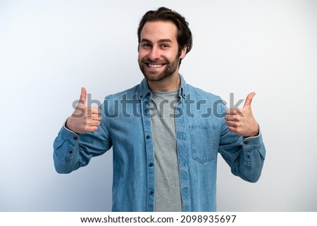 Young handsome man with beard feeling happy with big smile doing ok sign, thumb up with fingers, excellent sign. Stock photo 