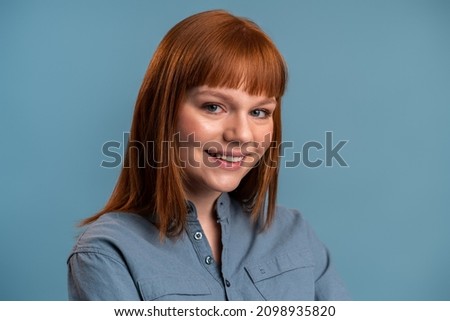 Close up portrait of pleasant smiling model with ginger beautiful straight unbinding hair isolated on the blue background. Stock photo 