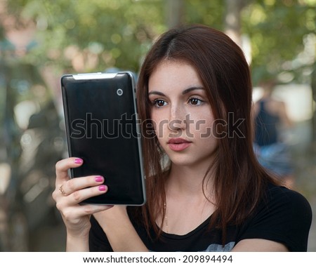 Brunette female student looking at screen of her tablet pc outdoors, young iGen woman is using digital tablet, mobile communications concept