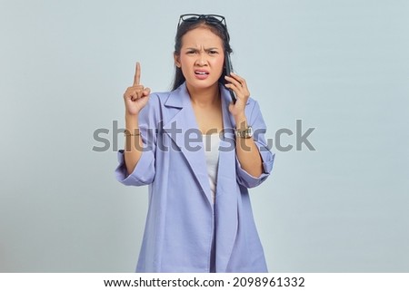 angry young Asian woman talking on cell phone and raising hands isolated over white background