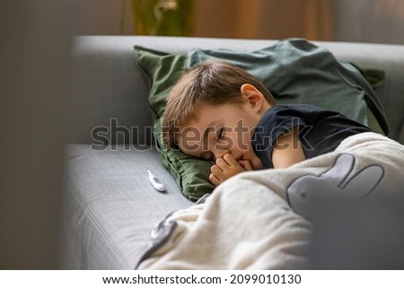 Unhealthy little boy child measure high temperature with thermometer sleep in bed relax at home in bedroom. Sick ill little kid suffer from flu fever asleep in bed on lockdown quarantine.