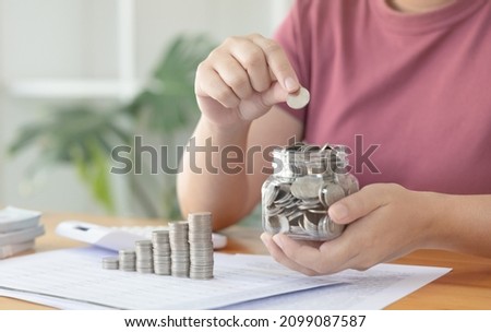Woman puts a coin dollar in a jar, Saving money for future growth and knowing how to manage your spending wisely, Saving money for business growth or long-term profitability. Royalty-Free Stock Photo #2099087587