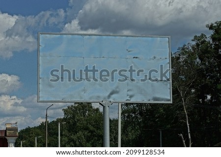 one large gray metal billboard on the pipe against the blue sky and clouds and green vegetation