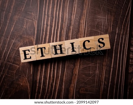 Wooden cube with word ETHICS on a wooden table background.