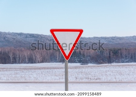 Road sign, Yield sign. Snow lies on the field, in the distance the forest. Winter, frosty morning.