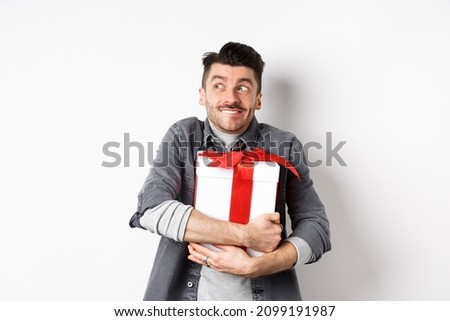 Happy boyfriend hugging gift from lover, looking aside at empty space and smiling excited, making romantic present on valentines day, standing on white background