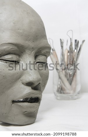 Female face in clay with artistic tools. Sculpture in process of creation, modelling of the head. 