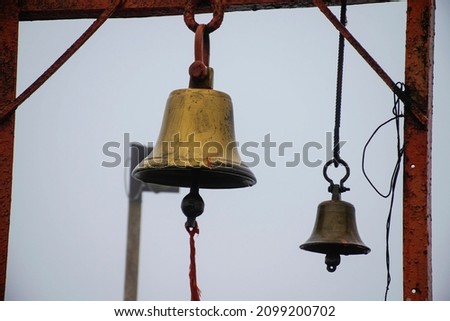 Stock photo of two ancient copper or bronze bell hanging on a orange color iron frame at Hindu temple on blur foggy background. Picture captured at sateri hill station Kolhapur ,Maharashtra, India.