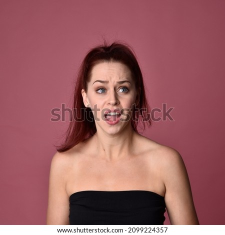 Head and shoulders close up portrait of pretty, red haired woman wearing minimal makeup and hairstyle,  with comical emotional facial expressions. Isolated on colourful pink studio background.