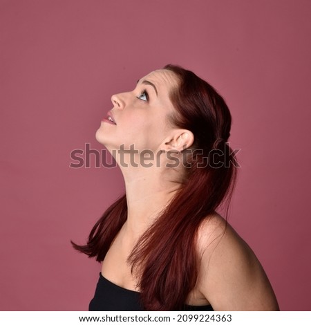 Head and shoulders close up portrait of pretty, red haired woman wearing minimal makeup and hairstyle,  with comical emotional facial expressions. Isolated on colourful pink studio background.
