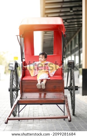 Asian cute little girl in Japanese traditional costume sitting on a rickshaw vintage style.
