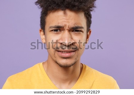 Close up of concerned worried young african american guy in casual yellow t-shirt posing isolated on violet background studio portrait. People lifestyle concept. Mock up copy space. Looking camera