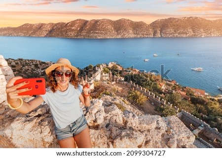 Tourist girl taking photos on smartphone of the scenic Kekova island from the Simena castle fort. Sightseeing and travel blogger in Turkey concept