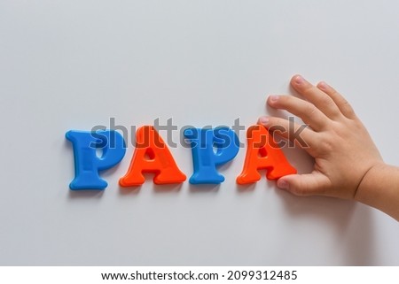 The word PAPA is made of colored magnetic letters typed by a child's hand. Early development of the child.