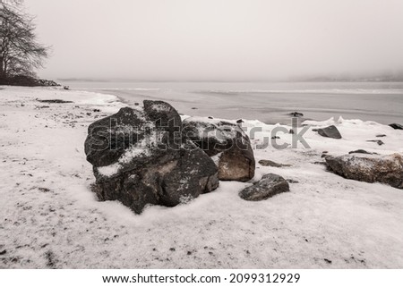 A foggy winter minimalist photograph of a snow covered beach with a boulder on it  