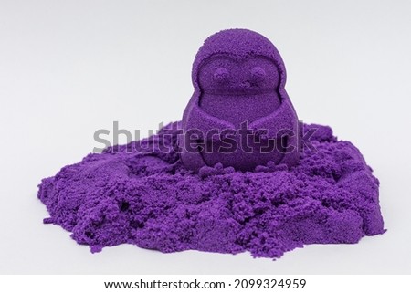 The figure of a penguin made of kinetic sand is purple on a white background.