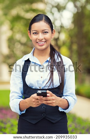 Portrait young, beautiful, smiling woman lawyer holding mobile smartphone. Multiethnic female professional in the city park, enjoying her work break. Positive human emotions, facial expressions 