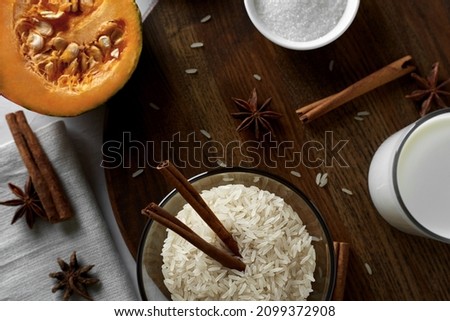 Rice grits and cinnamon sticks in a glass bowl. On the board - rice grits, cut pumpkin, cinnamon, sugar, milk and anise. Ingredients for milk rice porridge with pumpkin. Selective focusing. Flat lay