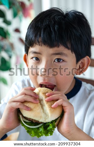 Asian boy taking a bite on his burger.