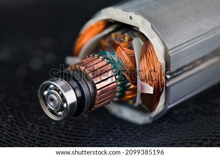 Rotor and stator detail of electric DC motor on black mesh background. Closeup of steel ball bearing, copper commutator or coil wires inside metal laminations of drill machine engine on dark blue net. Royalty-Free Stock Photo #2099385196
