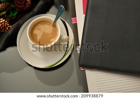 Coffee cup with eastern globe map made of bubbles, leather diary and a few journals on a coffee table