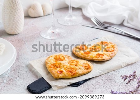 Two heart shaped pizzas on paper on a set table for valentine's day celebration