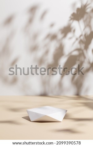 Abstract minimal nature scene - empty stage and polygonal podium on beige background and soft shadows of flowers and grass. Pedestal for cosmetic product and packaging mockups display presentation