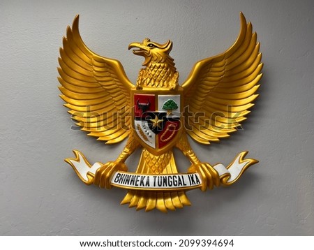image of a wooden statue of Garuda Pancasila, the Republic of Indonesia's national symbol. The meaning of Bhinneka Tunggal Ika is "Unity in Diversity". Royalty-Free Stock Photo #2099394694