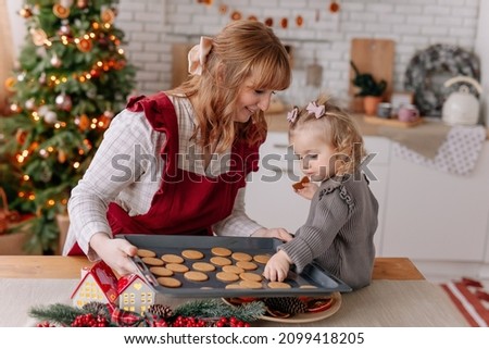Happy smiling Mother and daughter baking Christmas gingerbread cookies in decorated kitchen with natural fir tree. Organic orange chips decor. Family time, childhood and helping. lifestyle