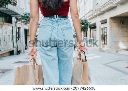 Back view rear view of a woman holding shopping bags while wearing cool style cloths. Jeans and a top. Shopping street. Changing and buying gifts concept.