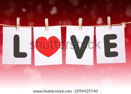Close up of love word with heart symbol on white papers hanging on the rope in blurred sparkling lights background