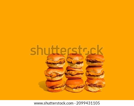 Sliders with cheese (mini hamburgers). Nine sliders on wall with solid yellow background. Plain hamburger bun