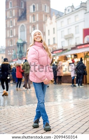 A girl stands in the center of the city, greets the new year. A blonde in a pink jacket walks around the city in winter