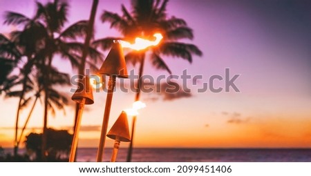 Hawaii luau beach party at sunset. Hawaiian tiki torches lighted up with fire at luxury resort hotel restaurant. Panoramic banner of hawaiian aloha spirit. Royalty-Free Stock Photo #2099451406