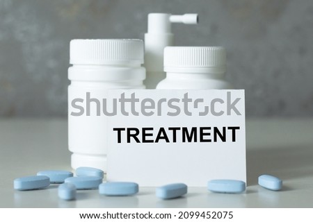 Treatment inscription on the card on the table next to white bottles of medicine and scattered blue tablets