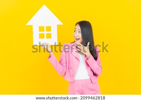 Portrait beautiful young asian woman with house or home paper sign on yellow color background