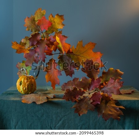 Branch with autumn leaves in a vase. Autumn colors on the leaves. Ripe small pumpkin.