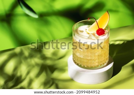 Whiskey sour trendy alcoholic cocktail with bourbon, lemon juice, egg white and ice, rocks glass on bright green background with hard light. Copy space Royalty-Free Stock Photo #2099484952