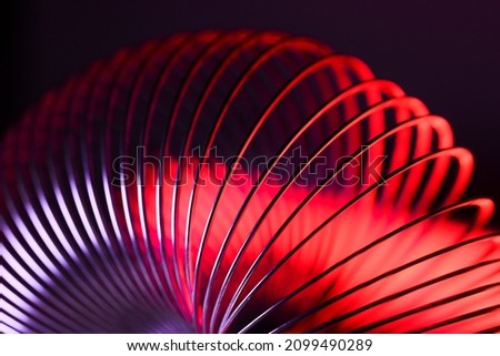 Closeup of coiled metal spring with sufficiently high strength and elastic properties in neon light over dark background. Macro photo, selective focus. Royalty-Free Stock Photo #2099490289
