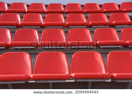 Plastic red chairs are arranged in straight rows in an empty sports stadium.