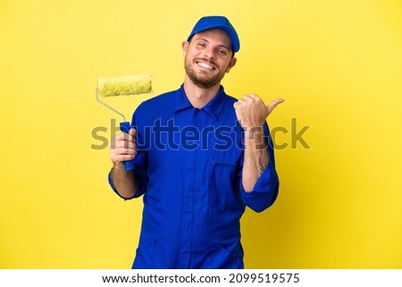Painter Brazilian man isolated on yellow background pointing to the side to present a product