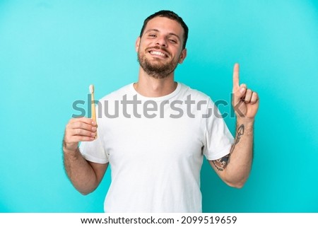 Young Brazilian man brushing teeth isolated on blue background pointing up a great idea