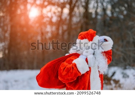 Santa Claus carrying Merry Christmas present gifts to children in a snow covered landscape 