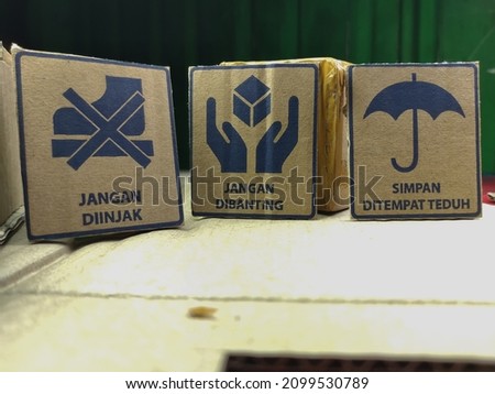 symbols on cardboard, shoes with a cross, hands and umbrellas, translation: don't step on it, don't slam it and keep it in the shade